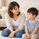 日本の家庭のリビングで、母親と幼い子どもが並んで座っている穏やかな日常シーン。