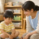 保育室で、夕方のやわらかな光の中、子どものそばに保育士が同じ目線で寄り添い、安心した時間を共有している様子