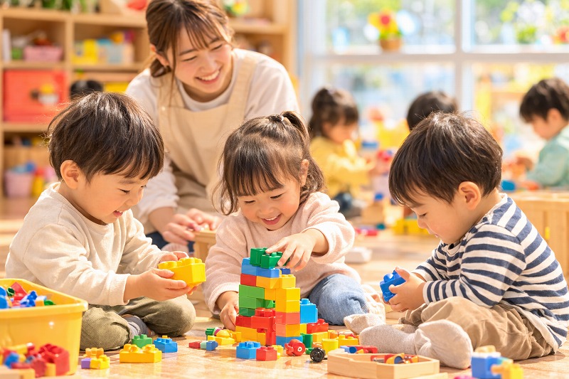 明るい保育室でブロック遊びを楽しむ園児たち。自然光が入る穏やかな保育園の室内風景。