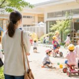 保育園見学で園庭や保育士の様子を確認している保護者と楽しそうに遊ぶ子どもたち