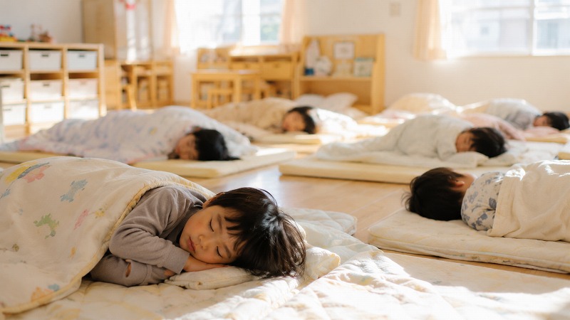 静かな保育室で布団に横になってお昼寝する園児たち