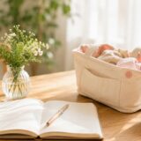 木製の机の上に速絡帳とベン、コーヒーや花が國かれた朝のワンシーン