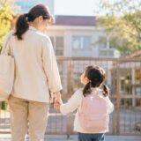 保育園の門の前で手をつなぐ親子