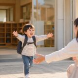 保育園の降園時、お迎えに来た保護者へ笑顔で駆け寄る子どもの安心した様子を写した写真風イメージ。