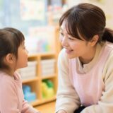 保育士が子どもの目線に合わせて話を聞き、安心して助けを求められる雰囲気の保育室の様子。