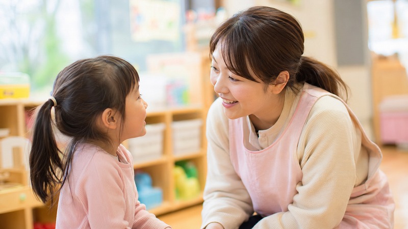 保育士が子どもの目線に合わせて話を聞き、安心して助けを求められる雰囲気の保育室の様子。